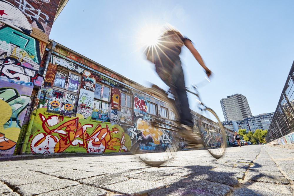 Ein Fahrradfahrer fährt auf das Ihme-Zentrum zu. Neben ihm auf einer Wand sind viele bunte Graffitis