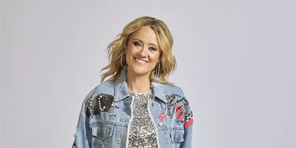 一位金色波浪卷发、面带微笑的女士身穿闪闪发光的银色连衣裙、绣花牛仔夹克和白色牛仔靴。