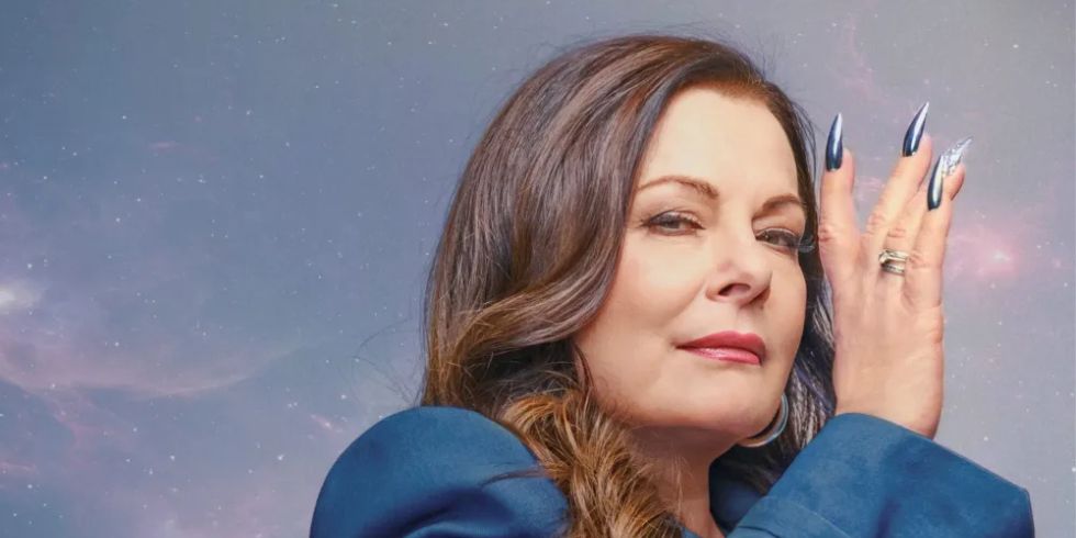 在宇宙背景下，一名身着蓝色服装、留着长指甲的女子神秘地看着镜头。