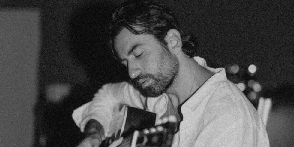 Man with closed eyes playing acoustic guitar in dark, atmospheric surroundings.