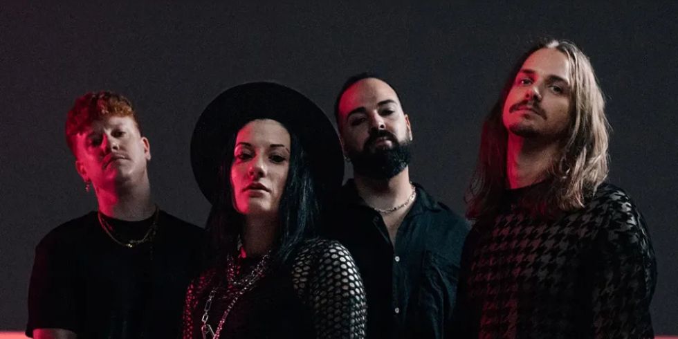 Four-piece band in dark clothing poses in front of a black background with a red light strip.