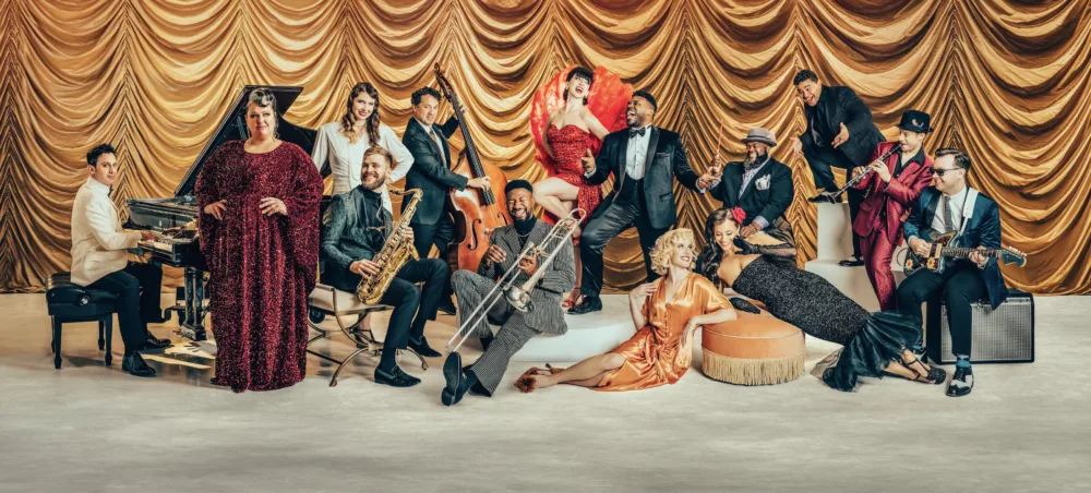 A glamorous jazz band with singers and musicians in elegant clothing poses in front of a golden curtain, surrounded by instruments.
