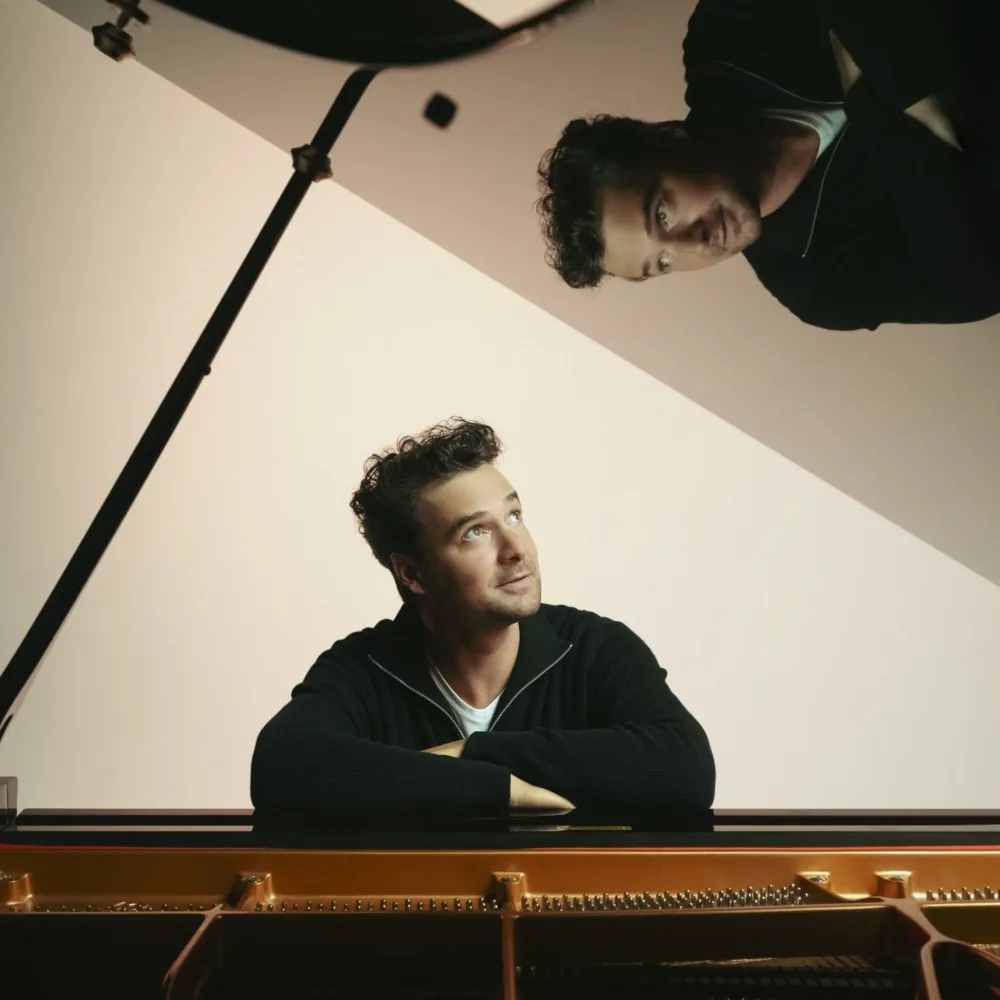 男子若有所思地靠在开放式三角钢琴上，钢琴盖上可以看到他的倒影。