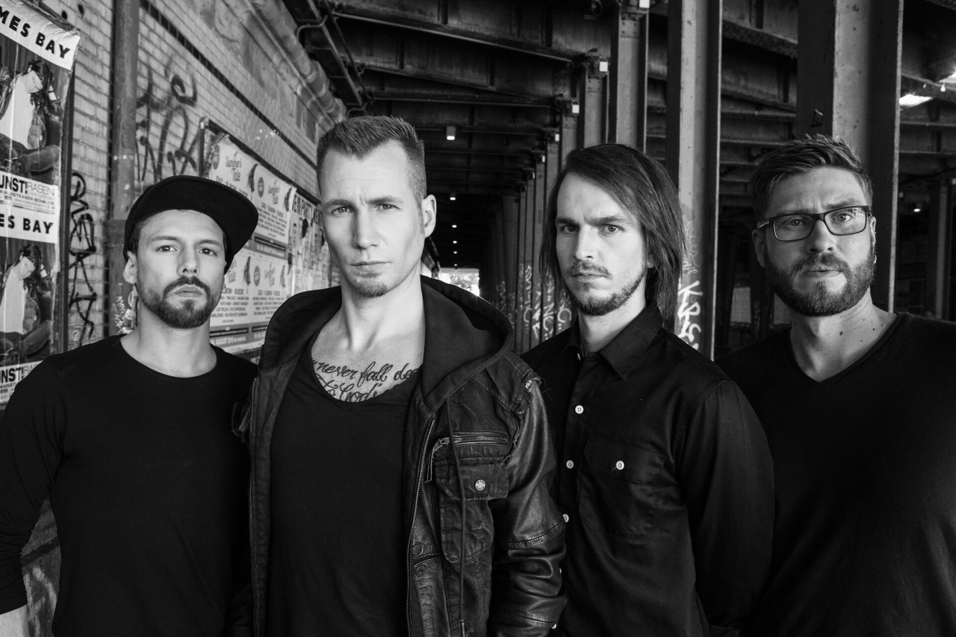 四人摇滚乐队在城市环境中一座涂鸦桥下摆出严肃的姿势。