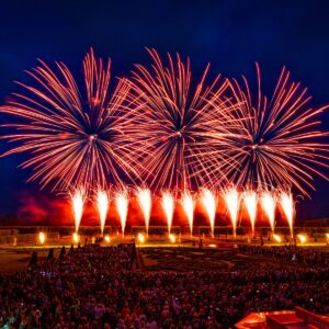 Spektakuläres Feuerwerk über barockem Garten mit großer Menschenmenge unter nächtlichem Himmel.