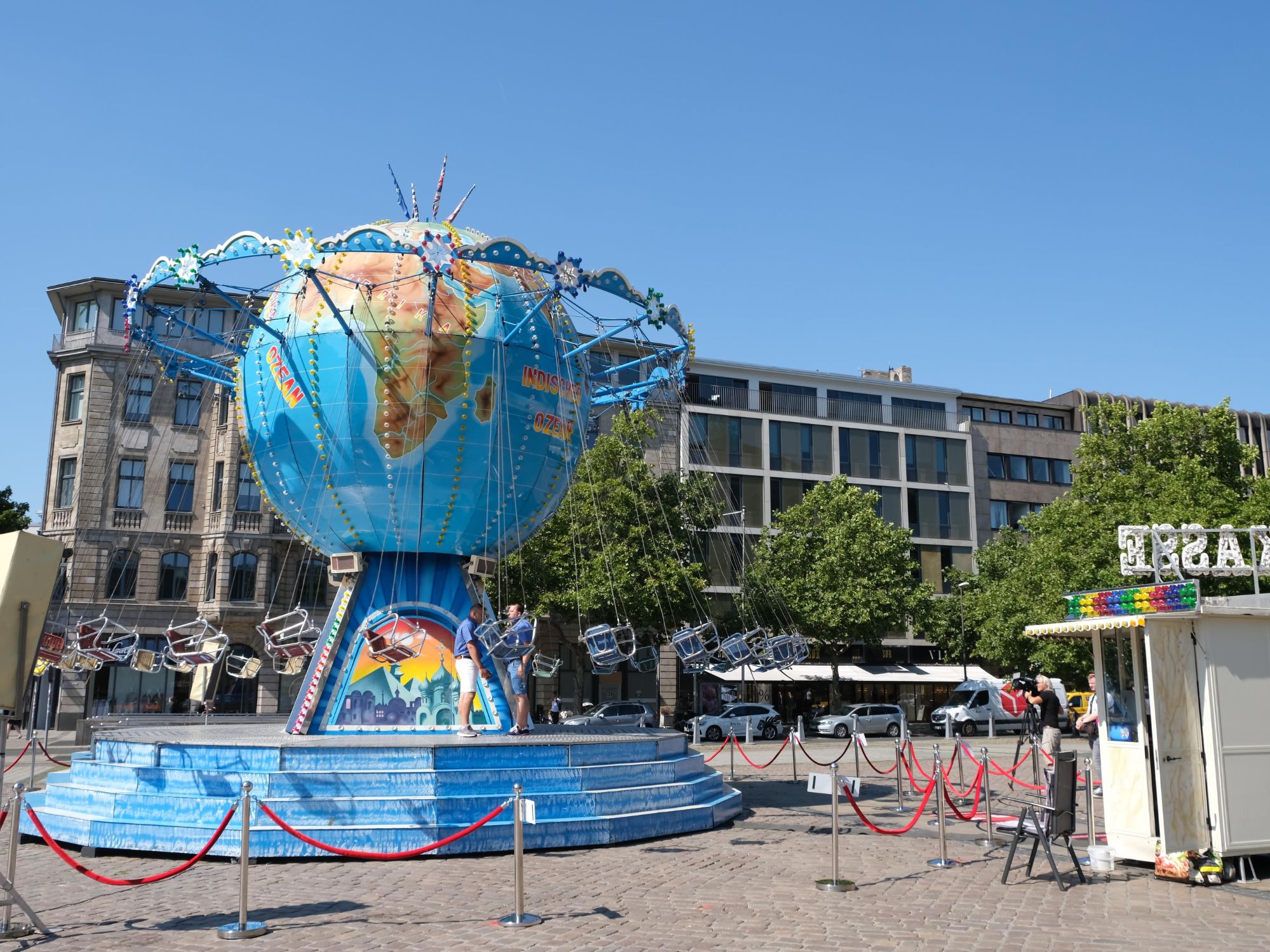 Globe-shaped chain carousel with ticket booth on a square in the city centre in sunny weather.