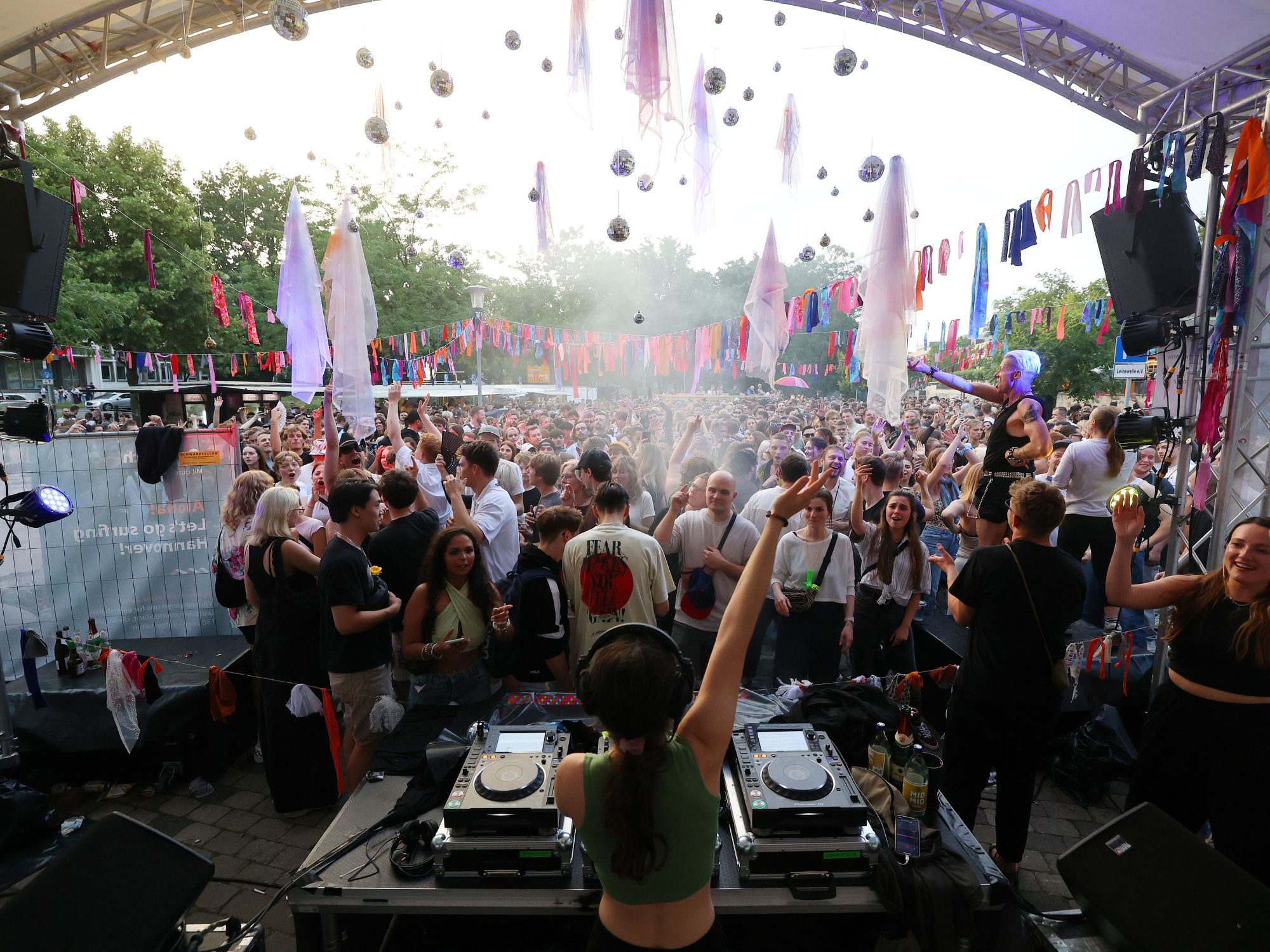 露天派对上有 DJ、翩翩起舞的人群、色彩缤纷的装饰和欢快的露天氛围。