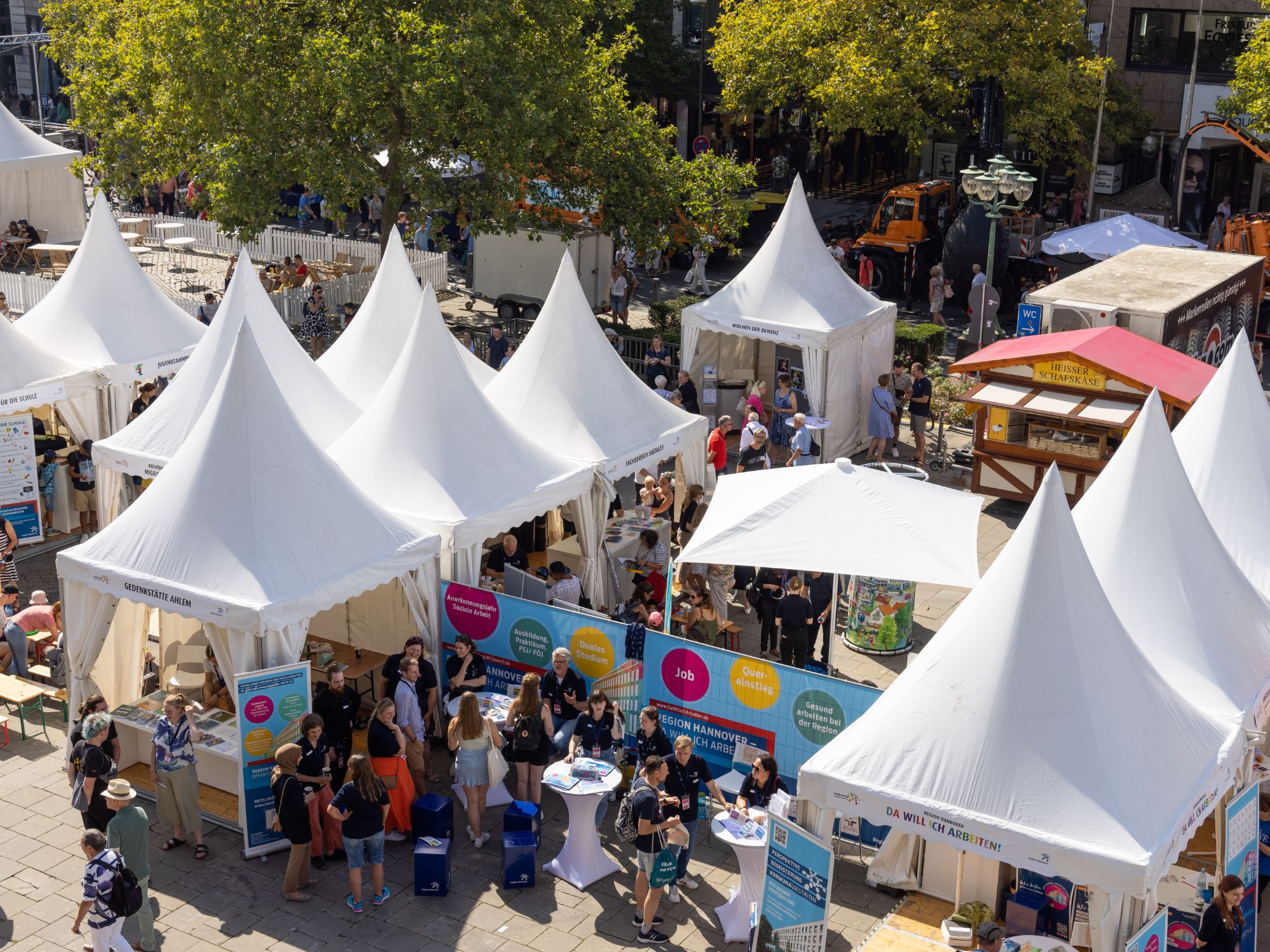 View from above of densely packed white pavilions with information stands and the public in the city centre.