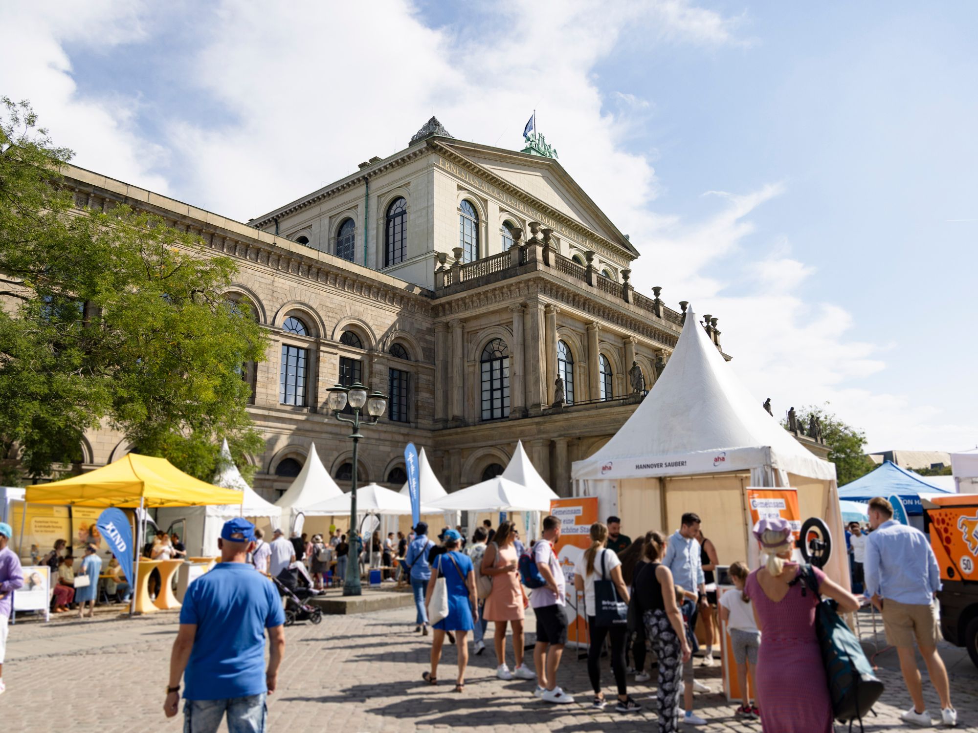People stroll between white tents and information stands at an event at Hanover Opera House.