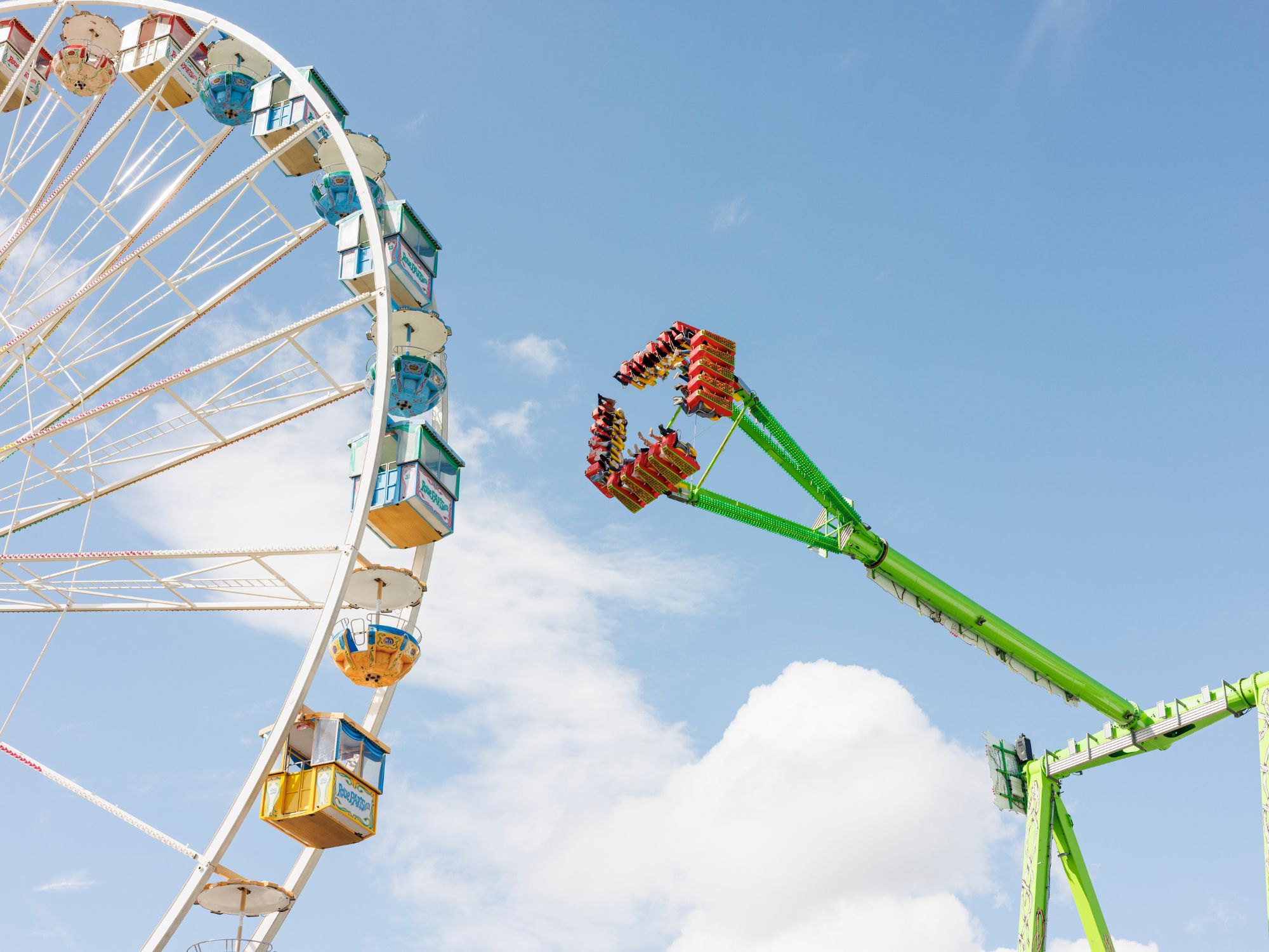 Ferris wheel and green high ride in front of a blue sky on the fairground by day.