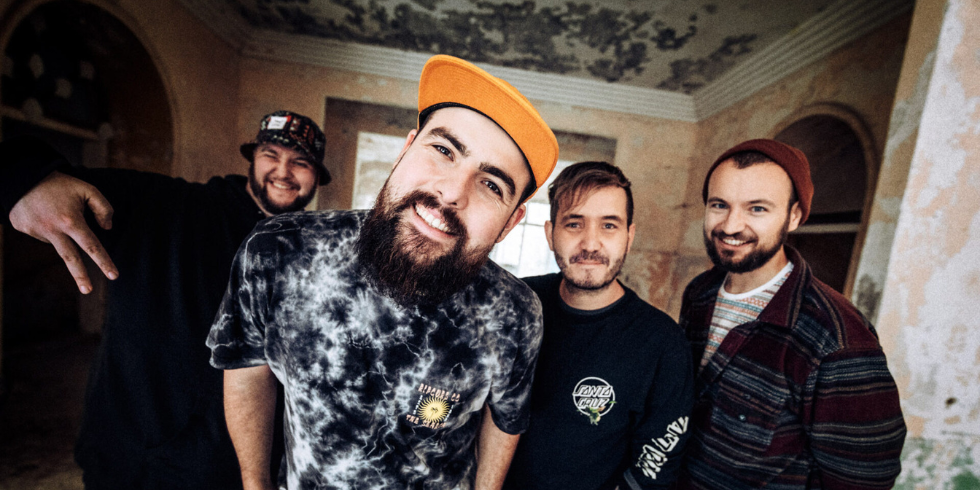 Four young men pose cheerfully in a dilapidated building and look directly into the camera.