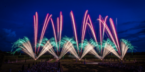 Farbenprächtiges Feuerwerk über barocker Gartenanlage bei Nacht, beobachtet von einer großen Menschenmenge.