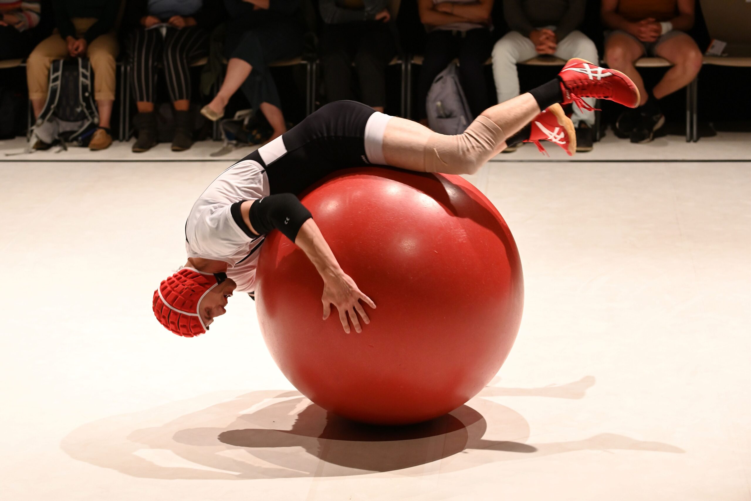 艺术家在观众面前进行舞台表演时,倒立在一个红色大健身球上保持平衡。